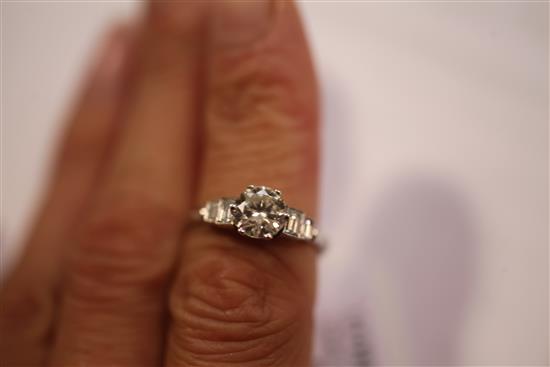 A platinum and single stone diamond ring with graduated emerald cut diamond set shoulders, size N.